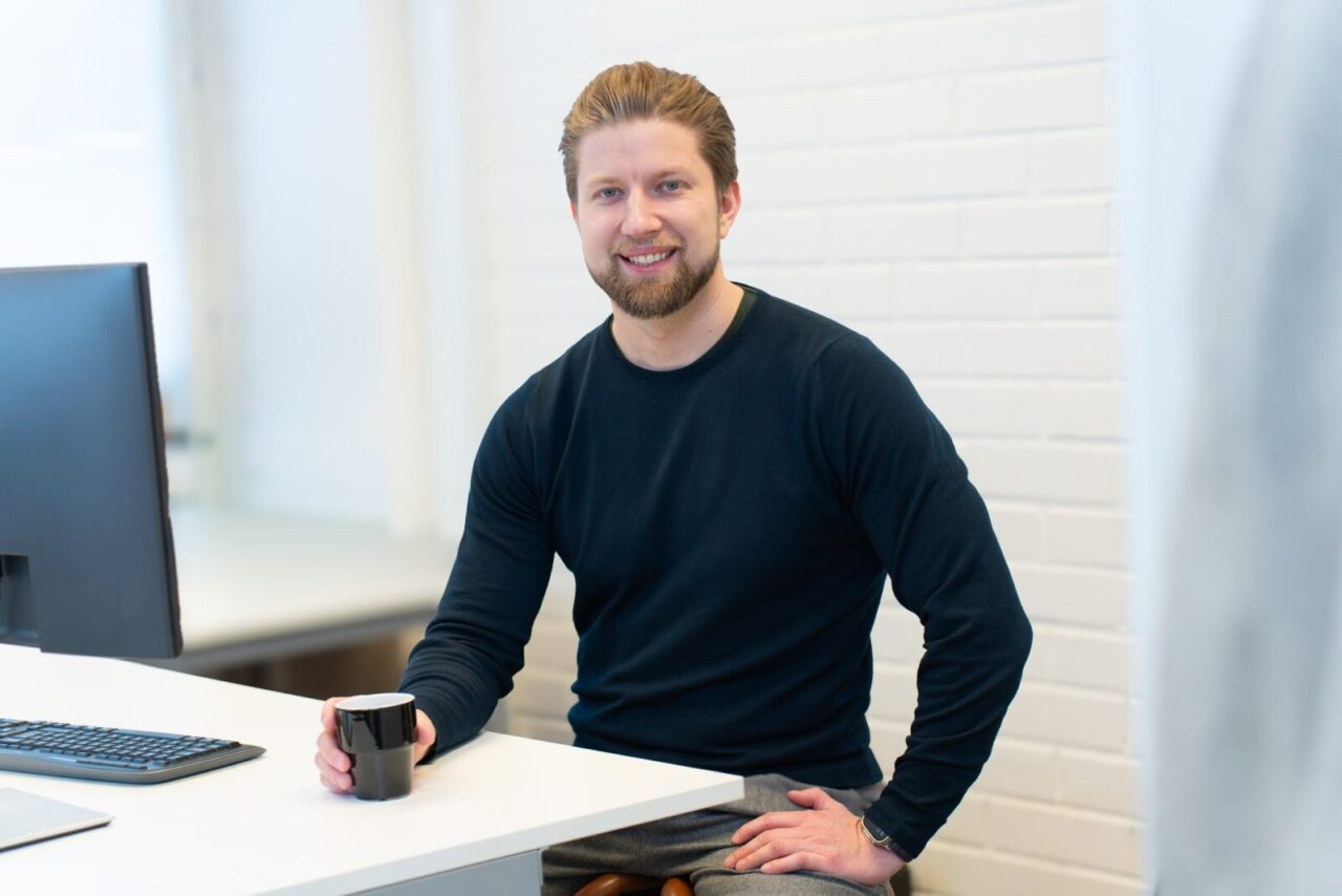 Toimitusjohtaja istuu työpöydän ääressä näytön edessä kahvikuppi kädessä.